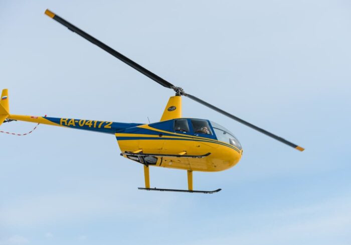 Желтый вертолёт Robinson R44 в полёте от компании "Captour"